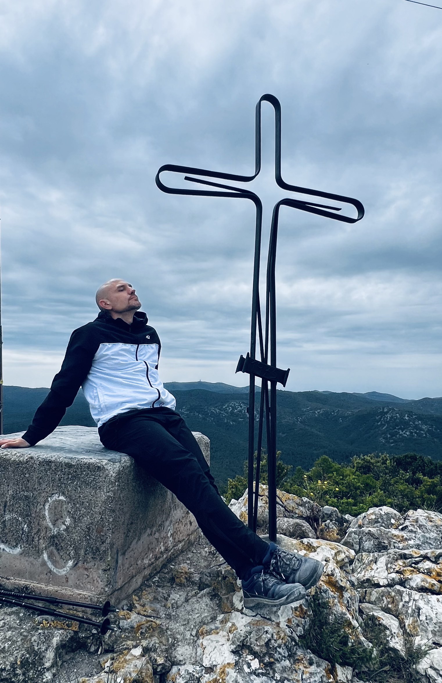 Iván Ramos sentado en la cima de una montaña junto a una cruz